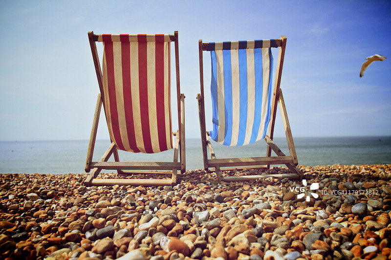 鹅卵石海滩上的蓝红色条纹沙滩椅图片素材