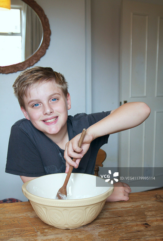 一个快乐的男孩在搅拌碗里搅拌混合物图片素材