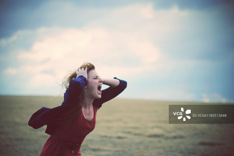 年轻女人在多风多云的田野里尖叫图片素材