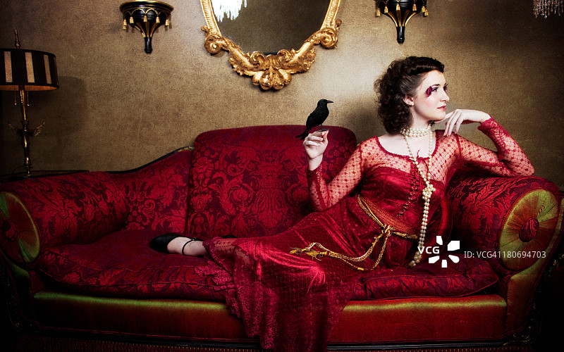 在带有黑鸟的红色古董沙发上的女人图片素材