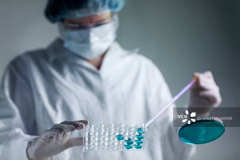 戴防护手套的研究人员用移液器处理绿松石色液体图片素材
