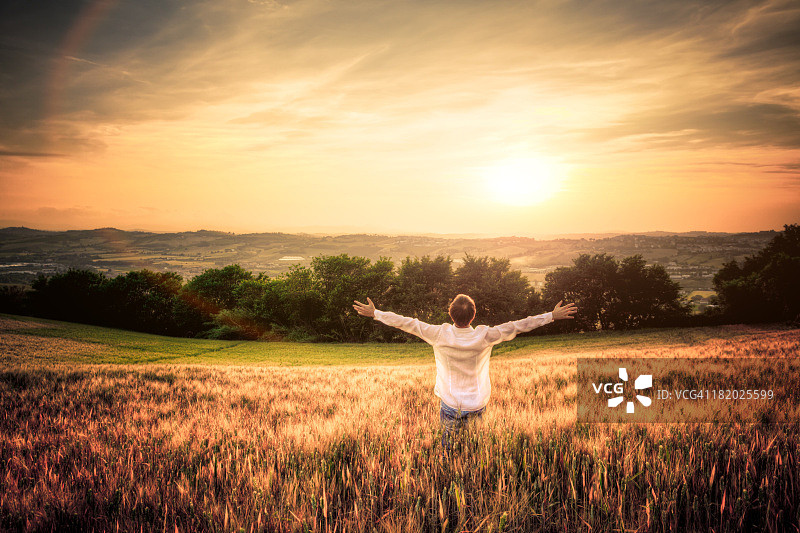 日落时分，麦田里张开双臂的男人图片素材