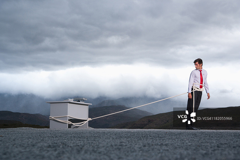 男人试图用长绳将办公桌拉到户外图片素材
