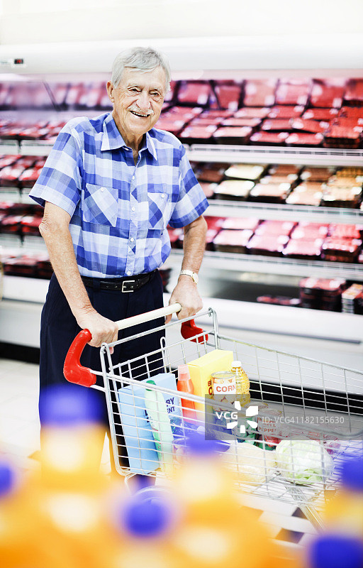 快乐的老年男人推着购物车经过超市冰柜图片素材