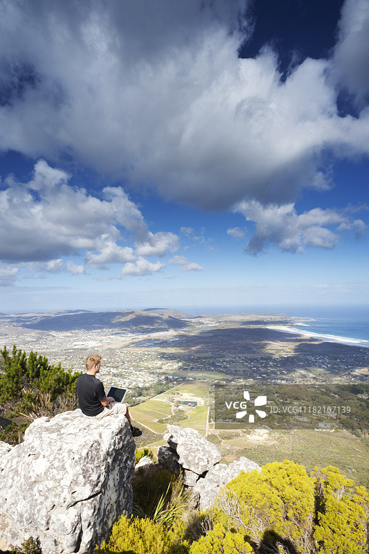 男人坐在悬崖边，使用笔记本电脑工作图片素材