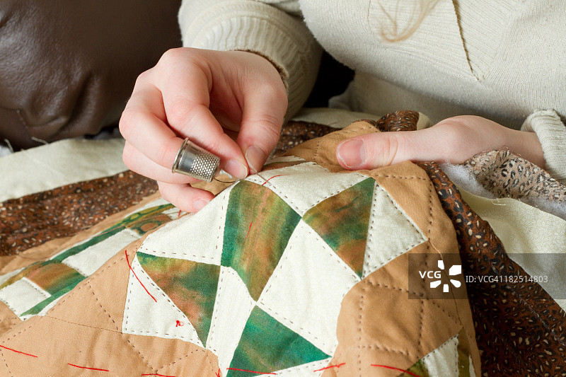 年轻女人的手，戴着顶针用缝纫针做绗缝图片素材