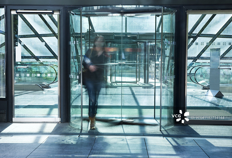 年轻女子穿过玻璃旋转门，动态模糊图片素材
