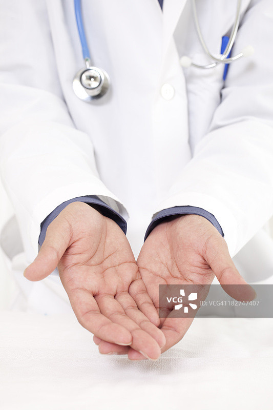 年轻的中东医生张开双手，身穿白大褂，戴着听诊器，表达关怀图片素材