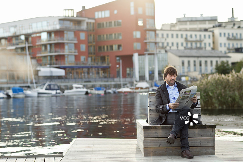 男子坐在水边读报纸图片素材