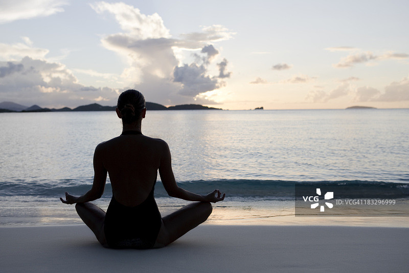 女人在日落时分的沙滩上练习瑜伽图片素材