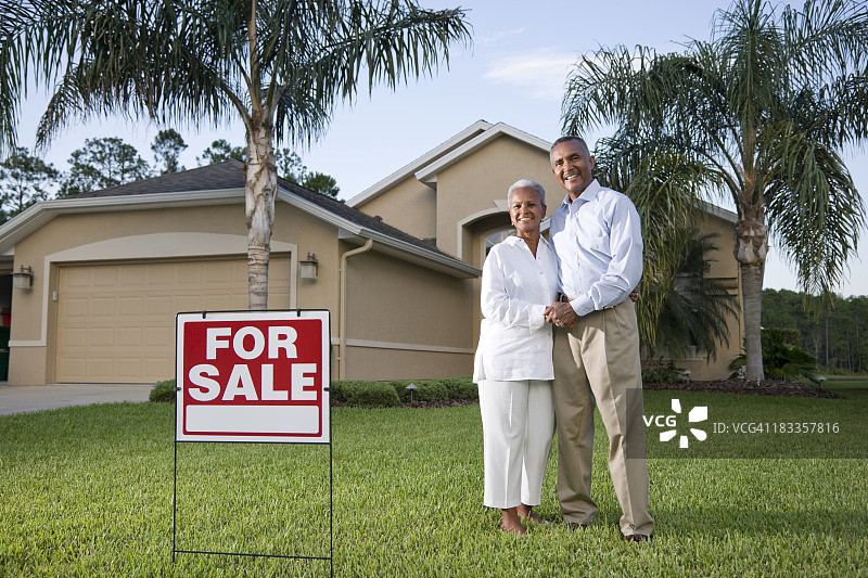 快乐的非裔美国夫妇在带有出售标志的房子外图片素材