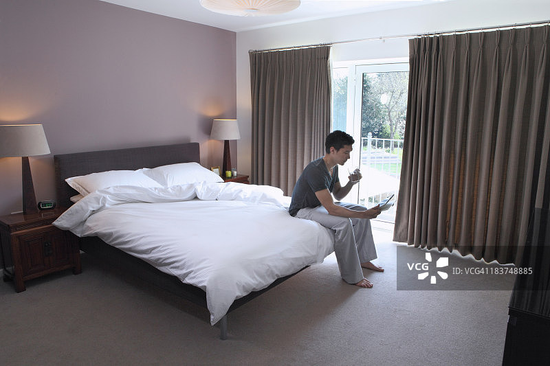 坐在床上看平板电脑的男人图片素材