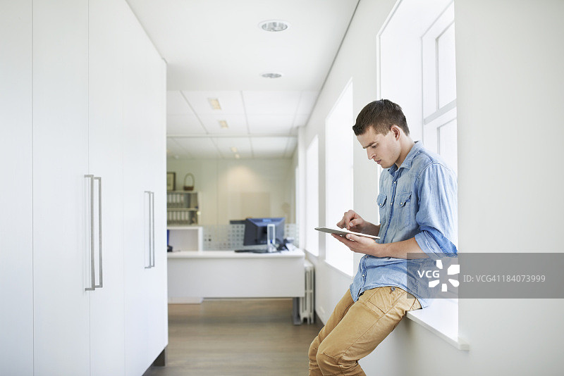年轻男人坐在走廊里使用平板电脑图片素材