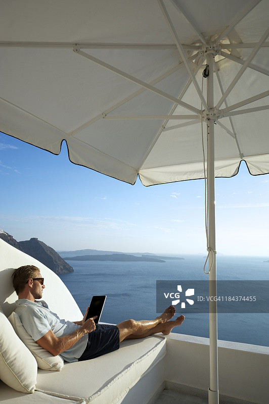 在海边阳台上放松的年轻男子使用数字平板电脑图片素材