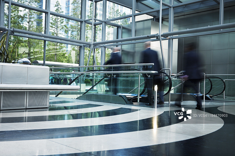 三位商人走向自动扶梯，模糊运动图片素材