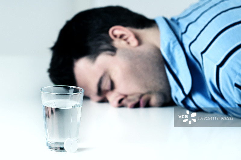 男人昏倒在玻璃杯和药丸旁边。图片素材