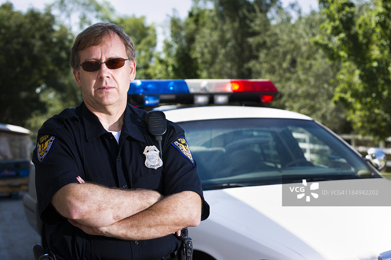 一名美国警察在警车旁摆出双臂交叉的姿势图片素材