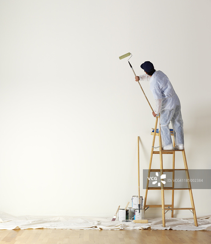 油漆工站在梯子上粉刷墙壁图片素材