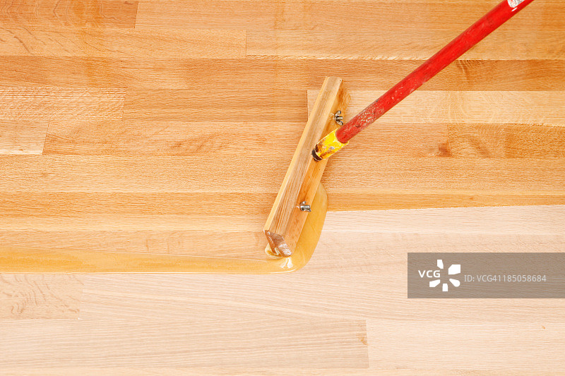 用刮水器式刷子将透明聚氨酯涂抹到硬木地板上图片素材