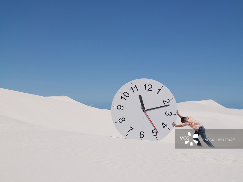 男子在沙漠中推动时钟图片素材