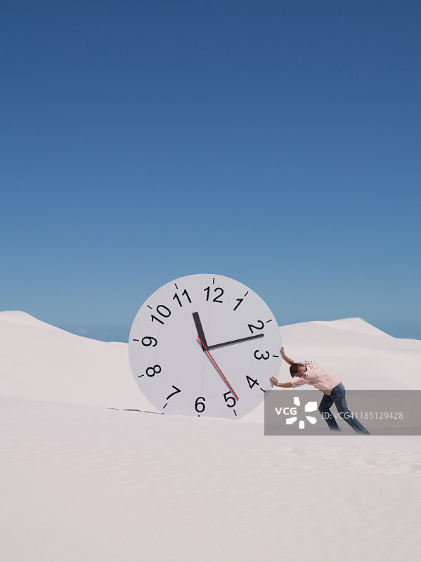 男子在沙漠中推动时钟图片素材