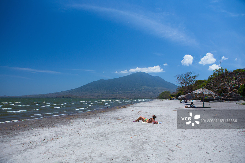 女孩躺在海滩上，前方是一座火山图片素材