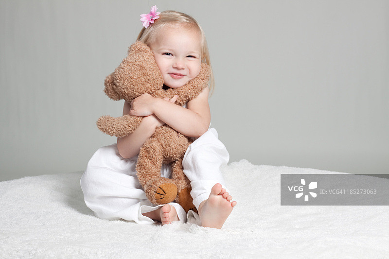 穿着白色连衣裙拥抱毛绒玩具的快乐小女孩图片素材
