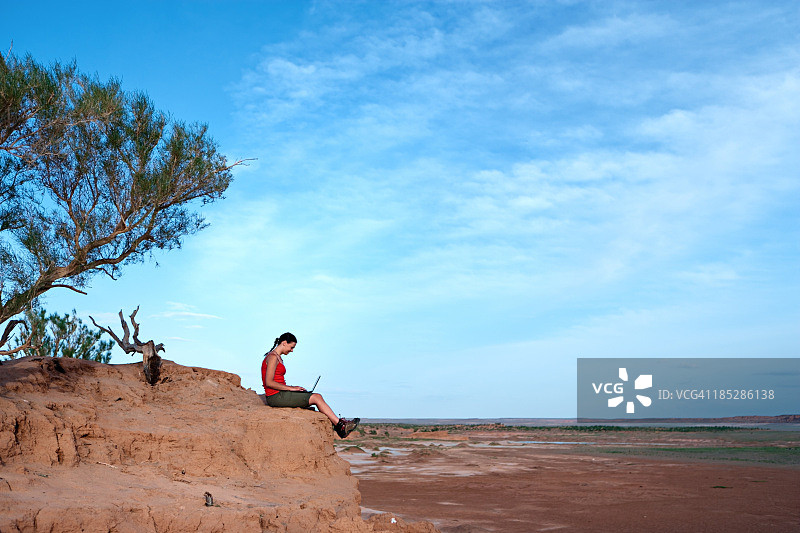 年轻女人在岩石上使用笔记本电脑图片素材