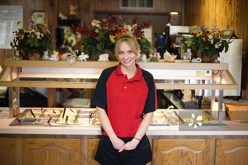 女服务员站在沙拉吧旁，双手放在围裙里图片素材