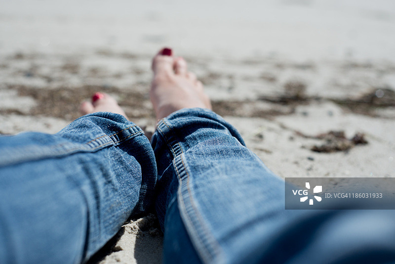 赤脚女人穿着牛仔裤在海滩上放松图片素材