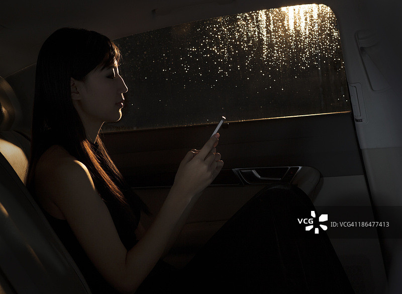 在北京的雨夜，坐在车里用手机发短信的年轻女人图片素材