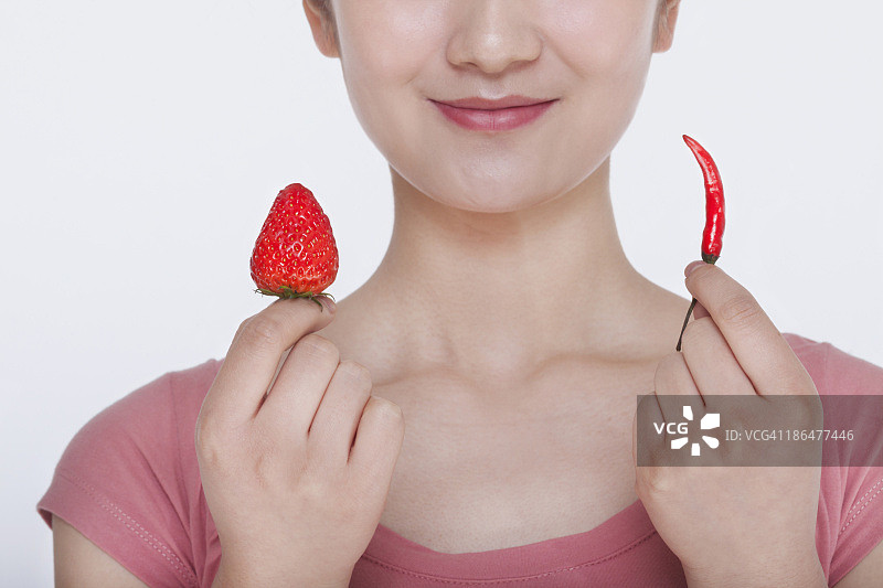 年轻女人手持草莓和辣椒微笑图片素材