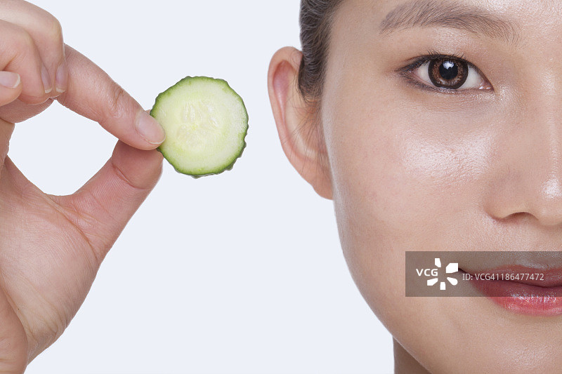 微笑的年轻女子拿着黄瓜片特写，影棚拍摄图片素材