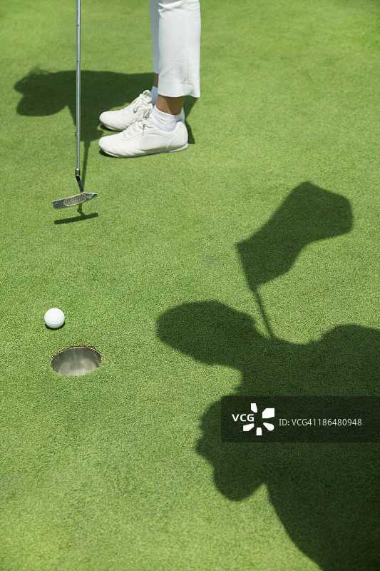 年轻女子在高尔夫球场击球，焦点在球洞图片素材