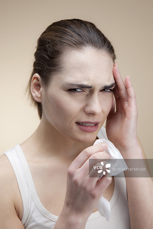 一位面容痛苦的年轻女人手拿纸巾按着太阳穴图片素材
