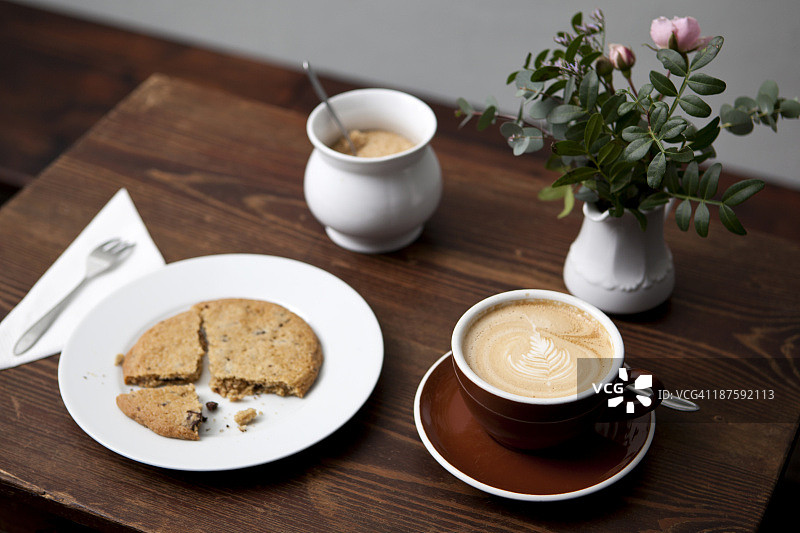 咖啡店桌上的曲奇饼、拿铁、糖罐和花瓶图片素材