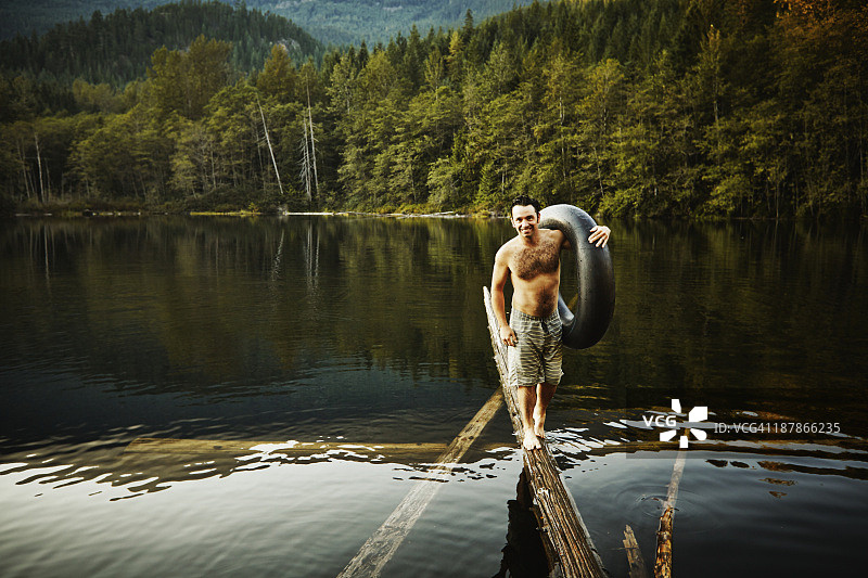 男人在湖中原木上保持平衡，手持内胎图片素材
