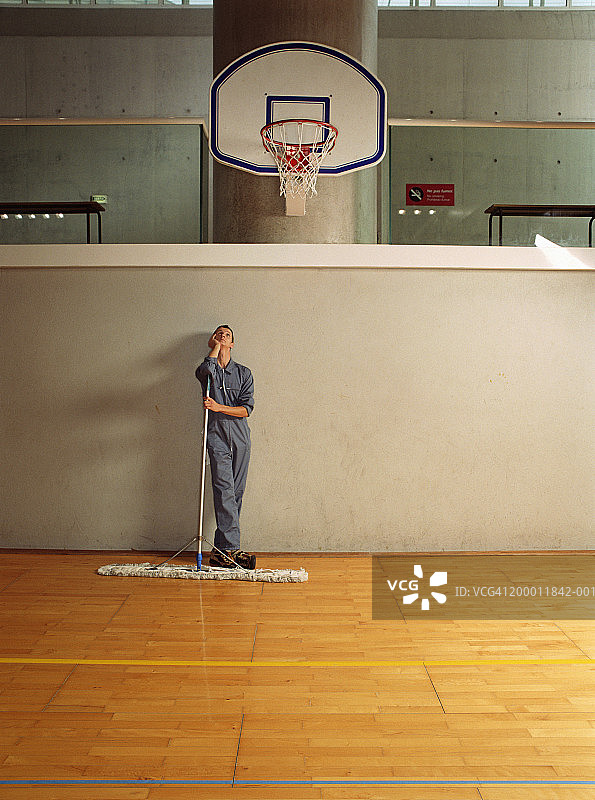 护理员倚靠在体育馆的扫帚上凝视着篮球框图片素材