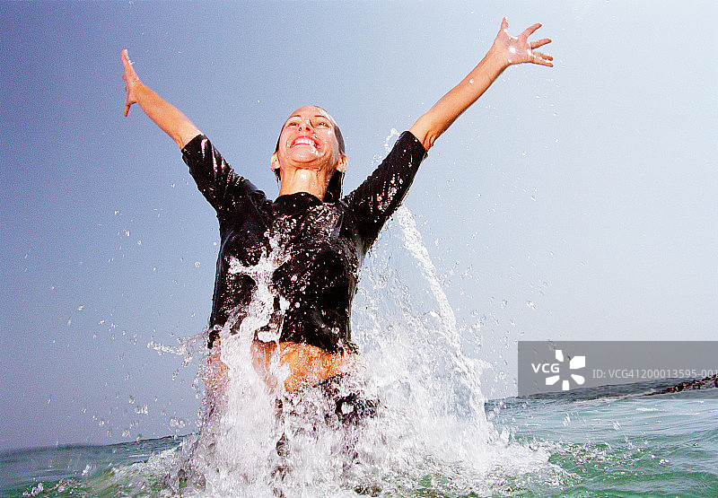 女人微笑着从海中走出，举起双臂图片素材