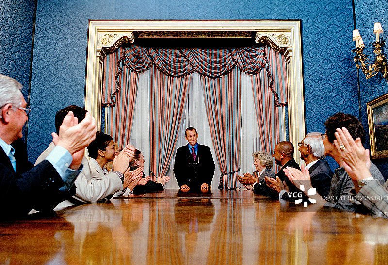 人们在会议桌前为男子鼓掌图片素材