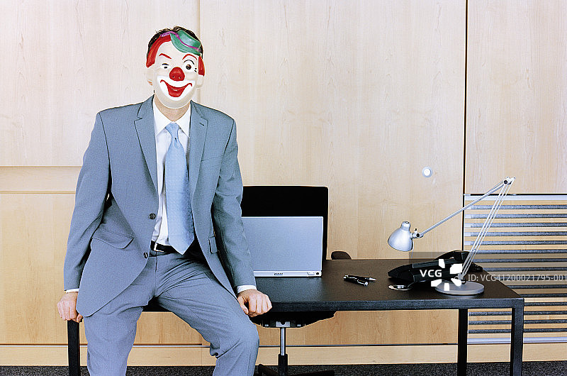 坐在桌子边缘戴着小丑面具的商人图片素材