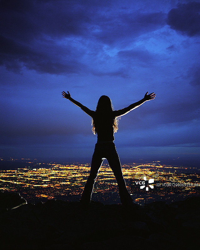 夜晚俯瞰城市，伸开双臂的女人，后视图图片素材
