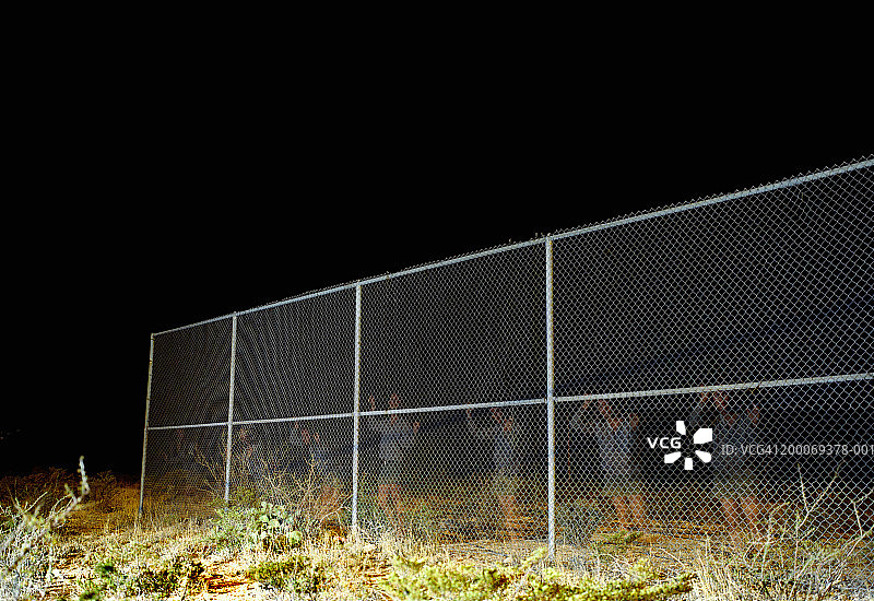 夜晚，女性隔着铁丝网观看（多次曝光）图片素材