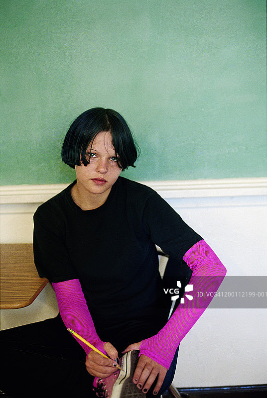 少女（13-15岁）坐在书桌旁，用铅笔在鞋子上写字图片素材