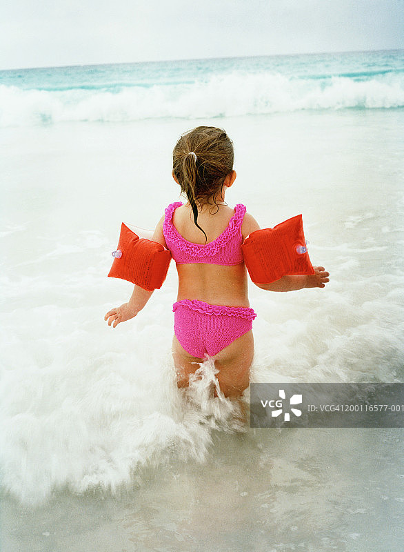 在海滩水中，穿着粉色比基尼的2-4岁女孩（后视图）图片素材