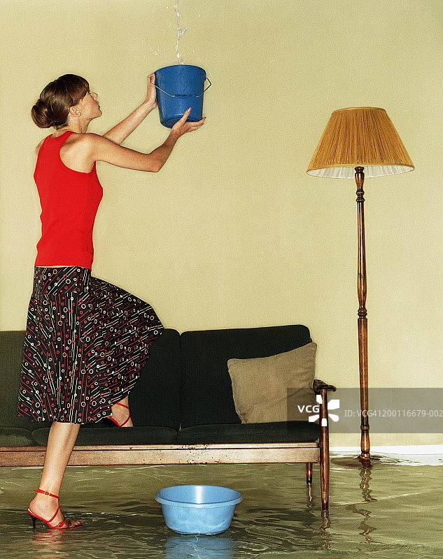 在被水淹没的房间里用水桶接水的年轻女人图片素材