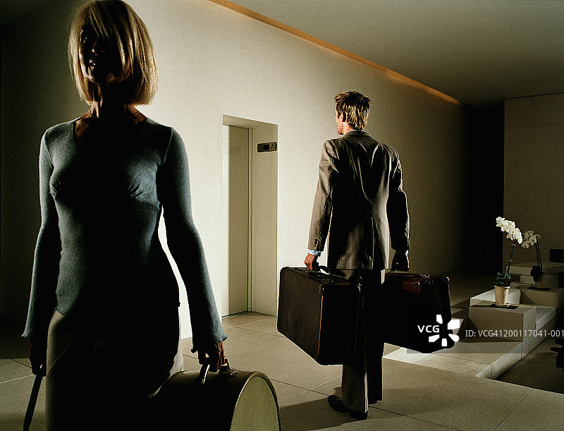 男女在酒店大堂里拿着行李，面朝相反方向图片素材