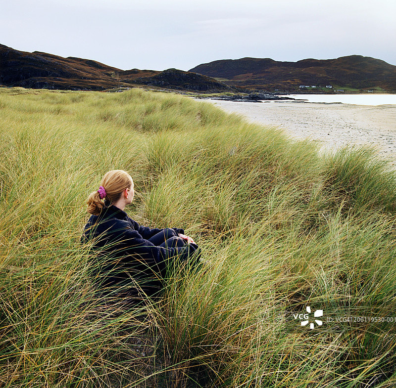 苏格兰高地，坐在草地上眺望大海的女人图片素材