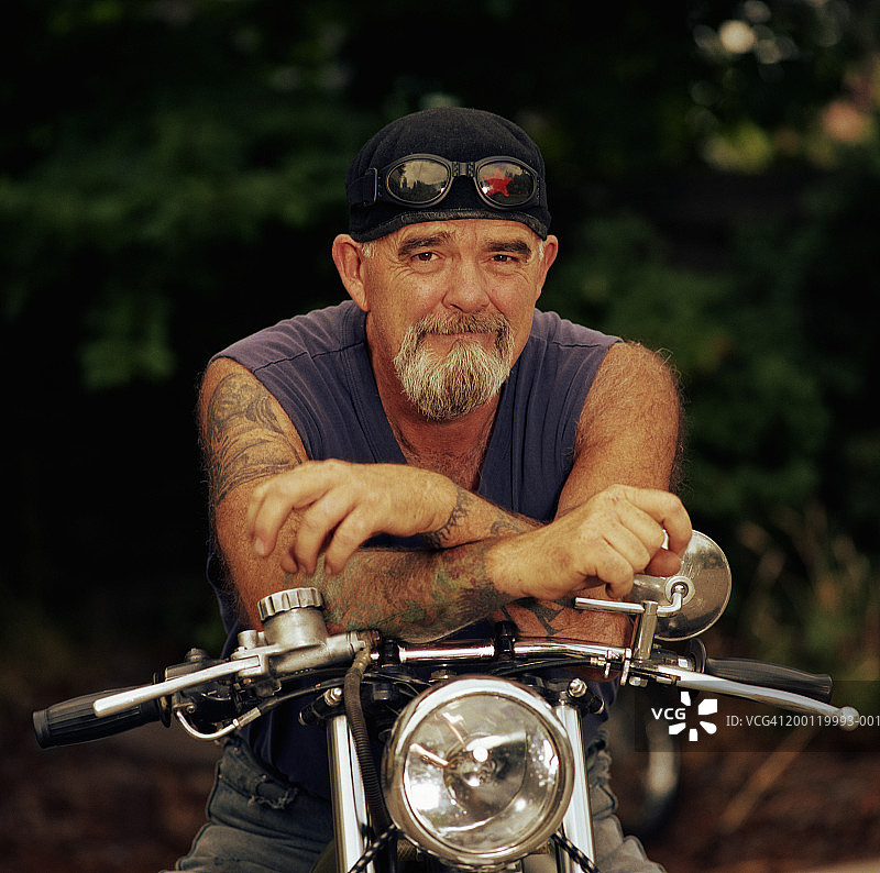 中年男人坐在摩托车上，靠着车把，肖像图片素材