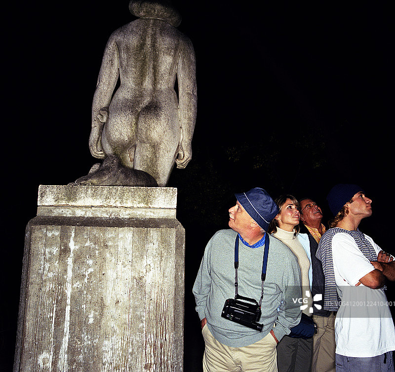 游客群体，中年男人观看雕像背面，夜晚图片素材